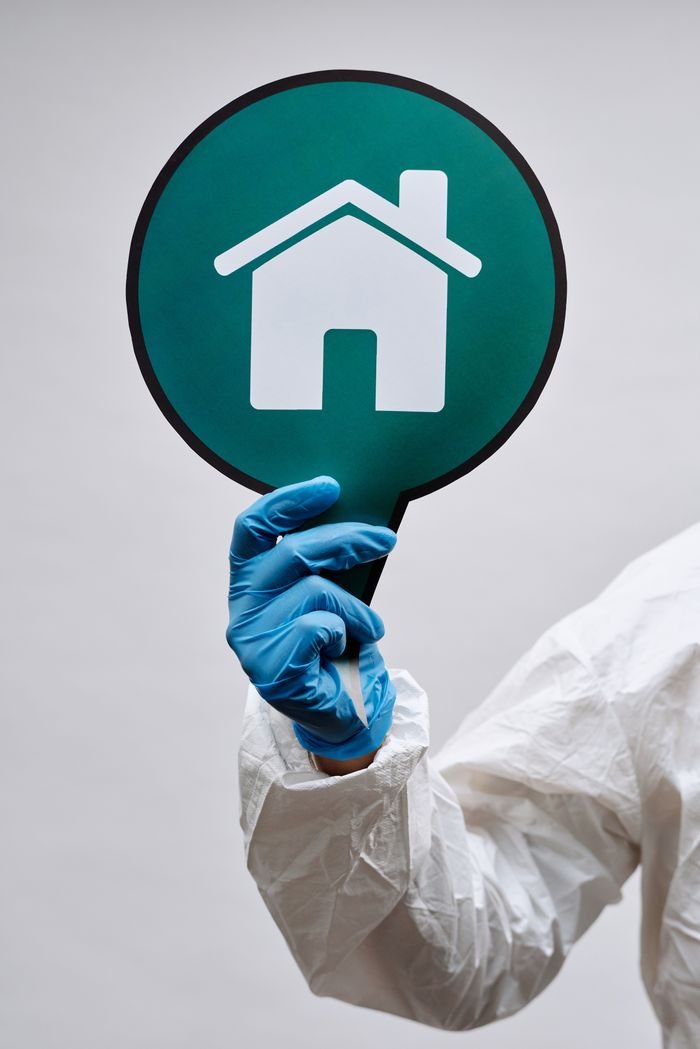 Close-up of a hand in protective gear holding a home safety placard, symbolizing stay-at-home message.