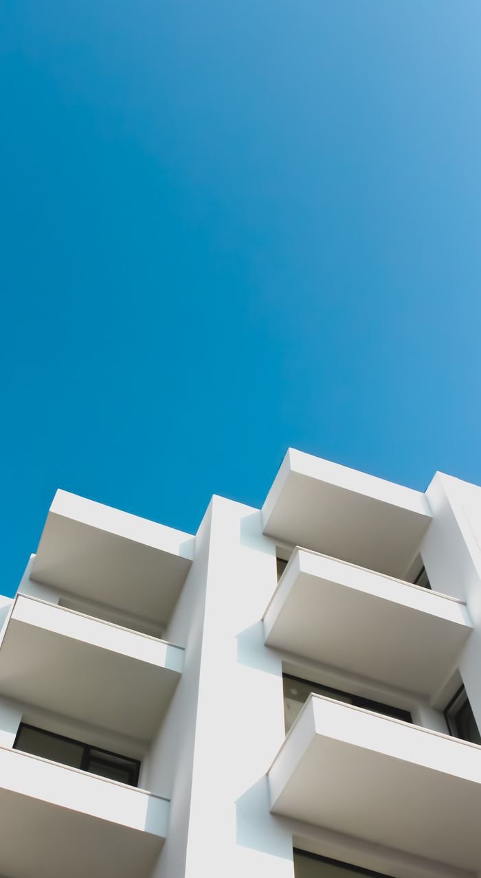 Low angle shot of a modern white building with balconies against a clear blue sky, showcasing architectural design.