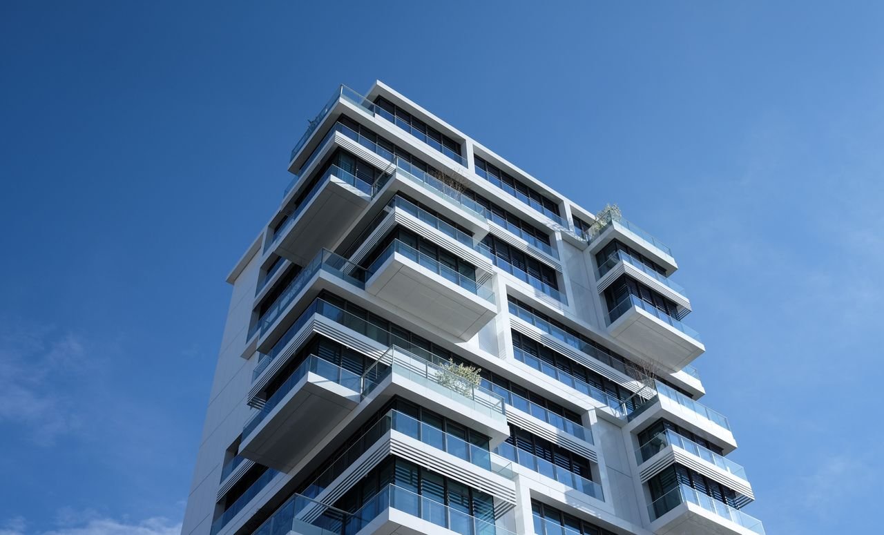 Striking low-angle shot of a modern condominium with unique balcony design and clear blue sky.